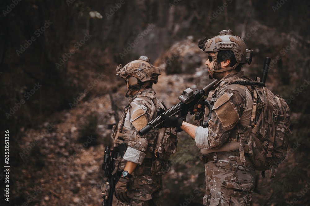 Fototapeta premium Two armed military operators secure an area during a tactical mission, holding rifles while patrolling a dense forest wilderness for defensive strategy, combat readiness, and national security.