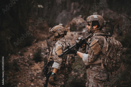 Schilderij op canvas Two armed military operators secure an area during a tactical mission, holding rifles while patrolling a dense forest wilderness for defensive strategy, combat readiness, and national security