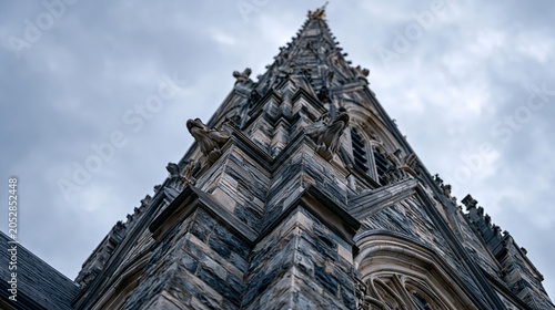 Gothic Revival church spire needle rising against overcast sky, dressed limestone ashlar courses tapering to ornamental finial, gargoyle water spouts projecting at corner buttress junctions, crocket