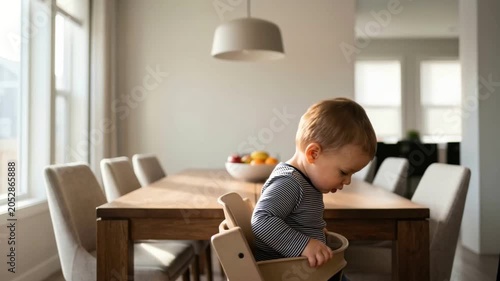 Mother lifting toddler son into high chair in dining room