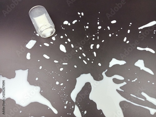 Milk spilled across a dark surface from an overturned glass. Creative food photography showing splash, liquid motion and accident concept with copy space.