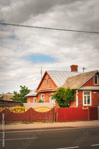 Quadro su tela red wooden house with ivy and decorative fence on cloudy day