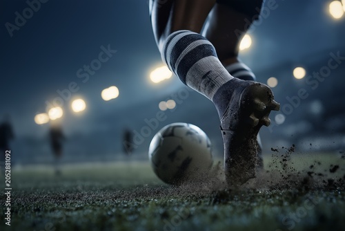 Dynamic close up of football player kicking soccer ball on illuminated stadium field during night match
