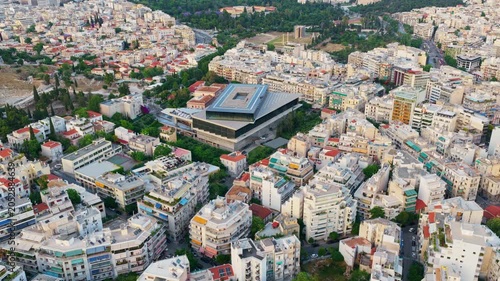 Golden hour drone footage flying over the urban landscape of athens, greece, showcasing the modern architecture of the acropolis museum surrounded by residential buildings and green spaces