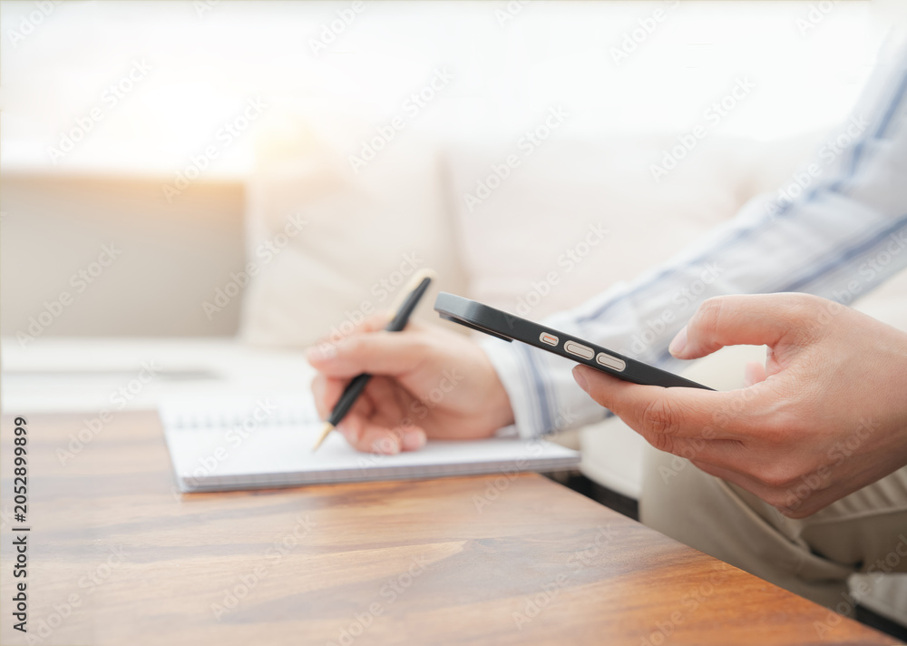 Fototapeta premium Professional reviewing CRM information on smartphone while taking notes. Email marketing, customer support, business software, workflow management, SaaS dashboard and remote work concept.