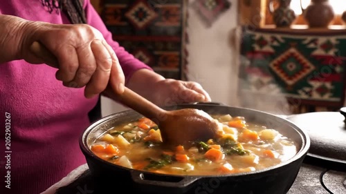 Hand stirring steaming vegetable soup in a pot on a stovetop, warm home kitchen setting with rustic textiles, cozy comfort food mood