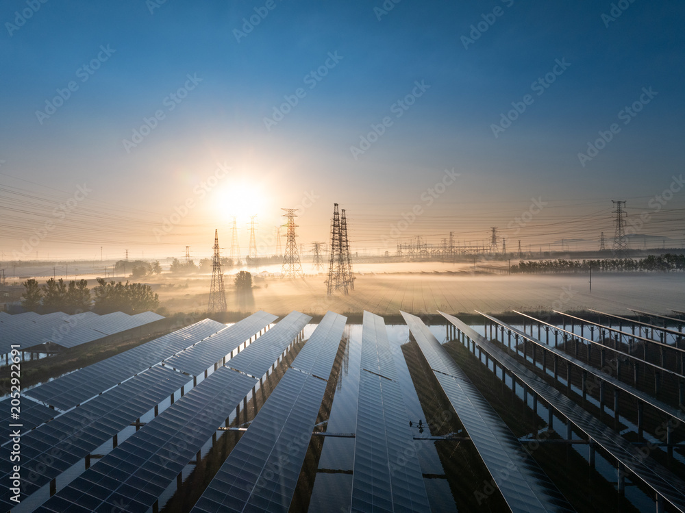 Naklejka premium Solar power station with transmission towers at sunrise over misty fields