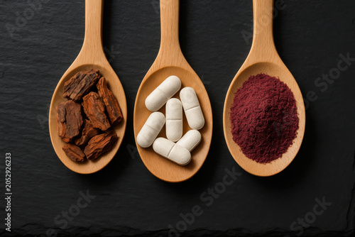 Three wooden spoon with supplement powder, capsule, and bark extract arranged on dark slate background for post workout recovery stack