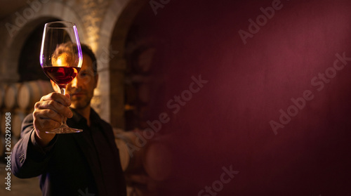 Man toasting with red wine in a cellar with wooden barrels  
