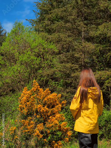 Fotografie Woman in yellow jacket stands before blooming bush with orange flowers