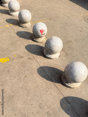 A row of small spherical granite bollards lining a pedestrian area in China, casting long shadows in the afternoon sunlight. These decorative stone barriers are commonly used in public spaces, plazas,