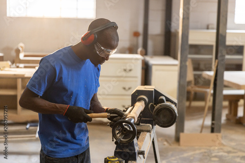 Lathe machine rotating and carving wooden spindle in workshop with sawdust on concrete floor