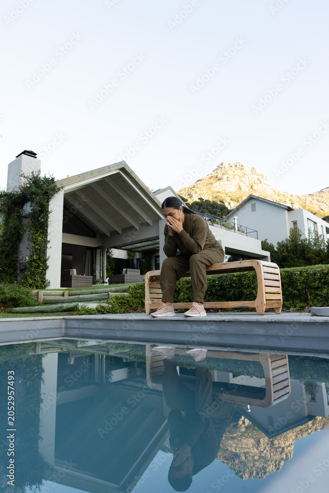 Fototapeta premium Curved wooden bench sitting at edge of still pool, covered patio seating and mountain reflecting
