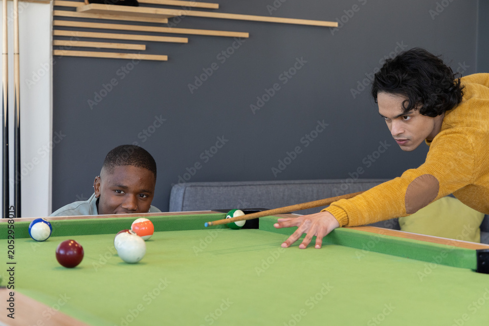 Obraz premium Diverse male friends playing pool at recreation lounge on green felt table with cue stick
