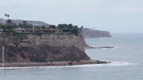 Sweeping overhead look at Palos Verdes Peninsula, capturing luxury real estate situated along rugged coastal cliffs, ocean waves meeting shoreline on overcast day