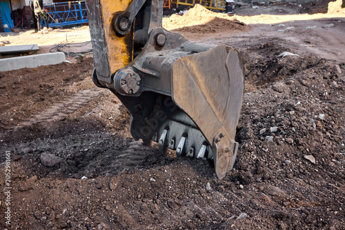 Obraz na plátně Excavator bucket digging into urban construction site soil