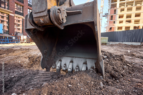 Excavator bucket digging into urban construction site soil