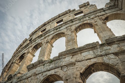 Photos The ancient Roman amphitheater in Pula, Croatia, showcasing its impressive stone arches and architectural details against a cloudy sky