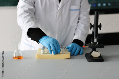 Scientist handling pharmaceutical vials near microscope in laboratory. Medical research, vaccine development, biotechnology testing and pharmaceutical industry concept. High quality photo