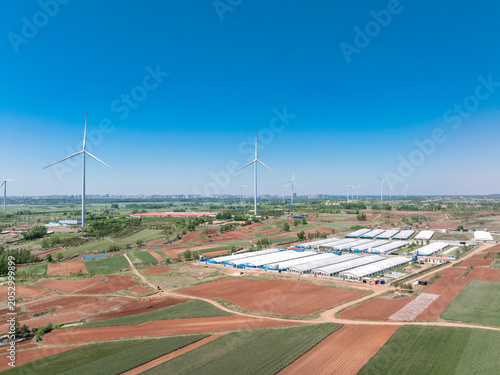 Fotografie Wind turbines and agricultural greenhouse fields under a clear blue sky