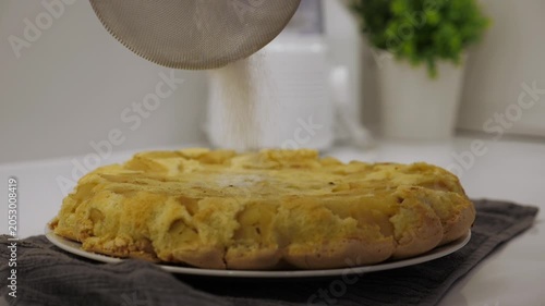 Cooking charlotte. Sprinkling powdered sugar on the pie. Freshly baked pie, finishing touch before serving. Closeup
