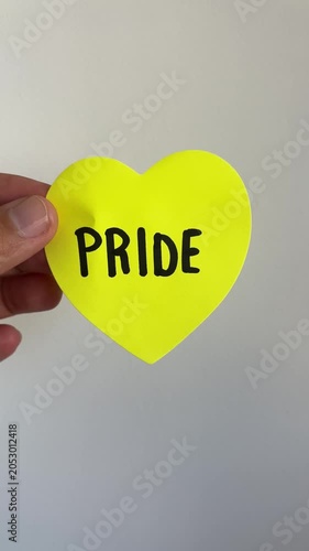 Hand holding yellow heart shape with Pride text on white background