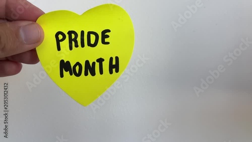 Hand holding yellow heart with Pride Month text on white background