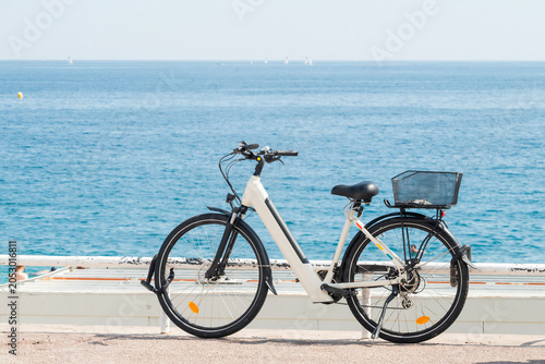 Modern electric bicycle parked on a sunny seaside promenade, overlooking the deep blue sea during a summer vacation.