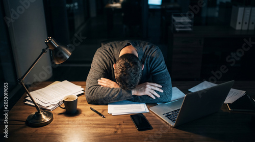 Burnout concept — exhausted man with head down on office desk, work stress and mental fatigue.