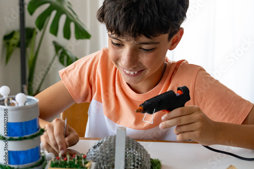 back to school. Teenager using a silicone gun and tweezers to make a project with recycled materials