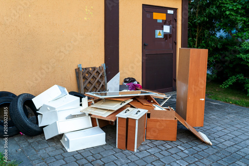 Tableau sur toile Pile of discarded cabinets, drawers, tires and broken furniture placed outside a residential building near a service door