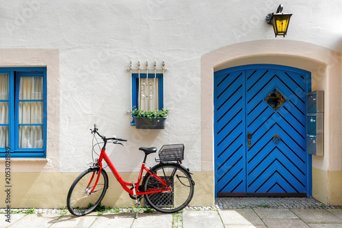 Red bicycle against the facade of a building with blue wooden door and windows in Fussen, Bavaria, Germany