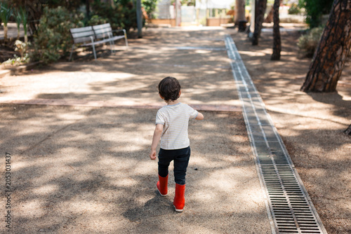 Young boy exploring park in red boots
