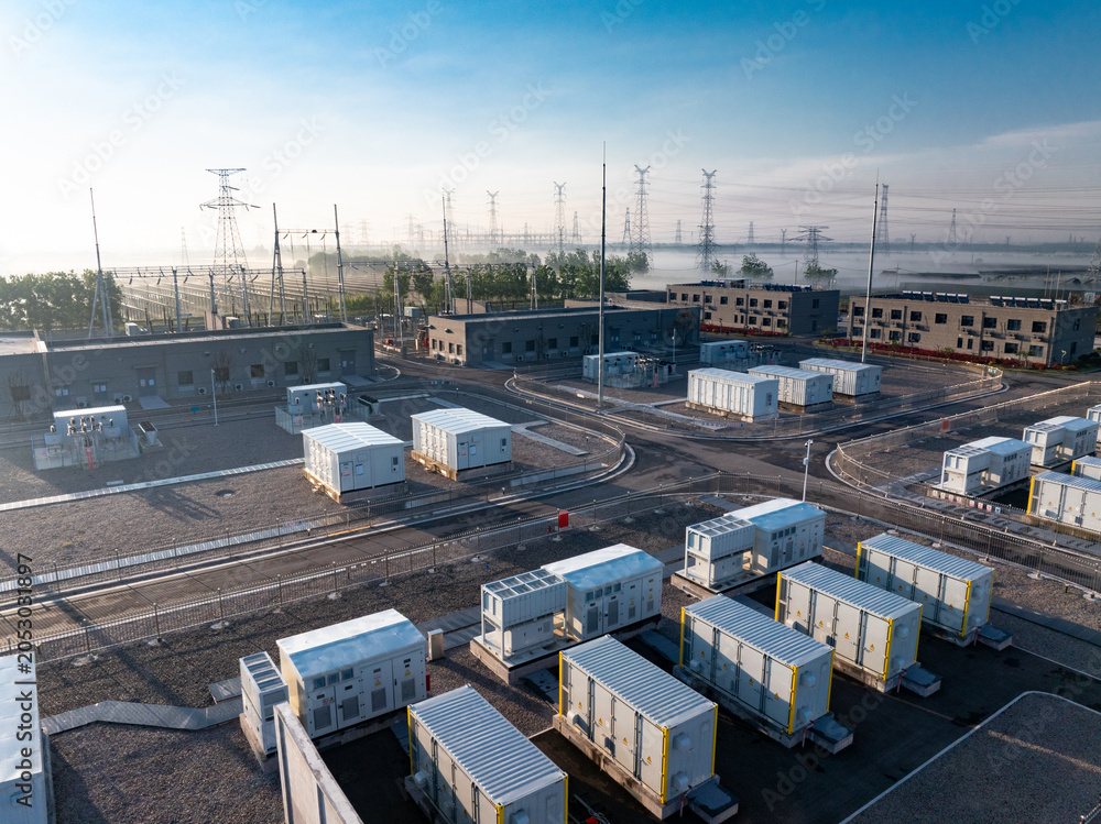 Fototapeta premium Power substation with energy storage containers and transmission towers under clear sky