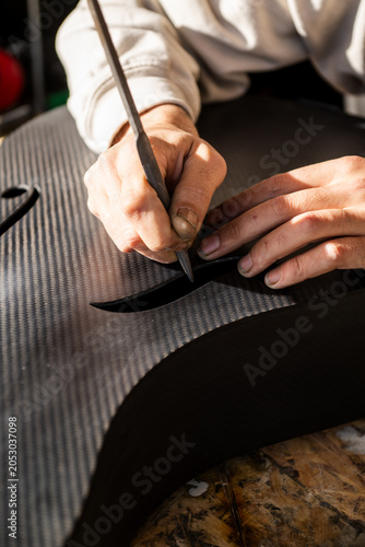 Close-up of Luthier Working on Carbon Fiber Cello Using Hand Tools in a Workshop Setting