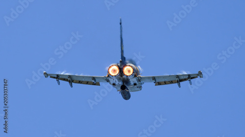 Tableau sur toile Military fighter jet with glowing afterburners performing high-speed maneuver beneath clear blue sky