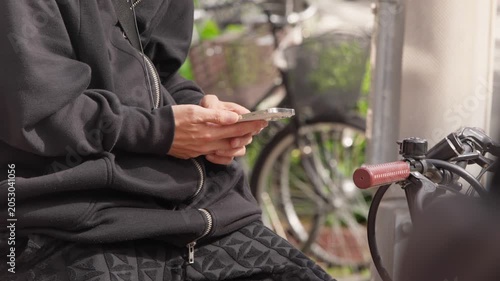 Slow motion Japanese man checks a smartphone while seated on a bicycle in an Osaka street, combining urban travel, communication technology and daily mobility in Japan