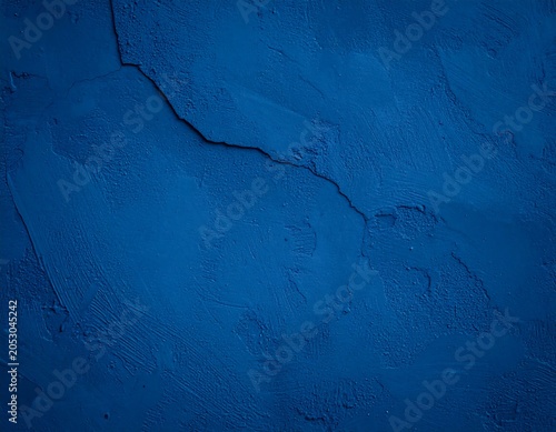 Deep blue textured backdrop of painted wall with rough, uneven surface and a prominent diagonal crack running across