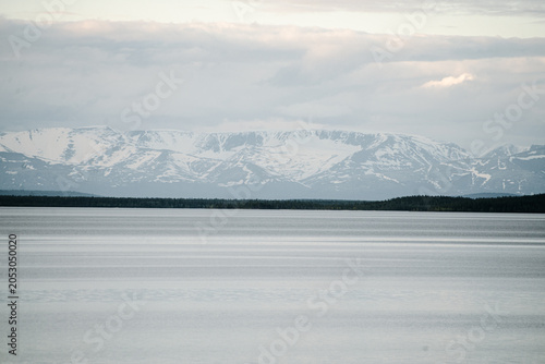 Calm lake with distant snowcapped mountains under overcast sky