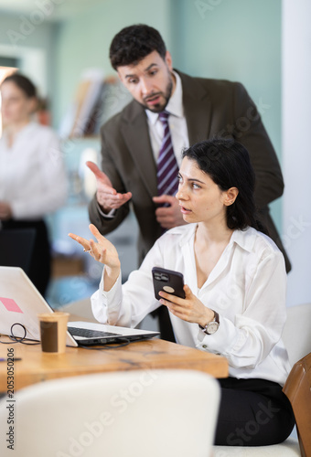 Fotografia Male boss chastises female subordinate for idleness and scrolling of phone, social networks and stealing personal and working time