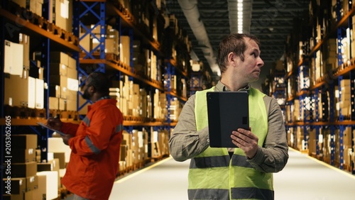 Fotografia Industrial depot with worker, coordinating cargo, dispatch with safety vest, warehouse staff manages packages and shipment details with tablet, large business operational performance