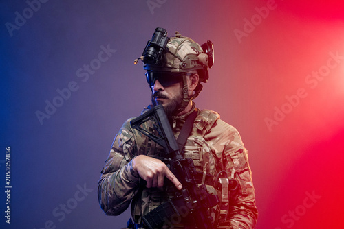 Obraz na płótnie Male soldier in tactical gear with helmet and night vision goggles holds an assa