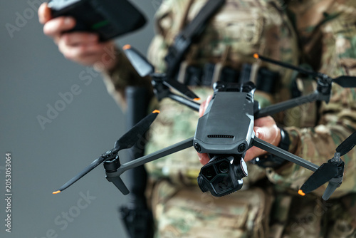 Foto Military serviceman in camouflage uniform holding a remote-controlled drone in neutral indoor environment