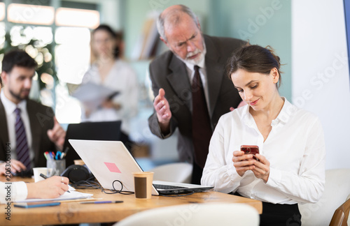 Obraz na płótnie Senior male boss chastises female subordinate for idleness and scrolling of phone, social networks and stealing personal and working time