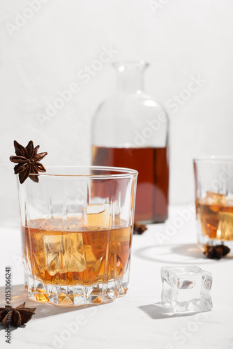 Cuadro en lienzo Whiskey glass with ice cubes and star anise garnish, decanter in background, alc
