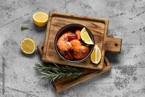 Foto Bowl of tasty boiled shrimps, rosemary, lemons and wooden boards on grunge blue