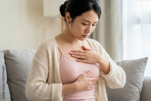 Worried young Asian woman checking her breast at home, Breast cancer self-examination concept.