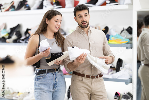 Foto Husband helps girl decide on choice of running shoes, shows suitable options, br