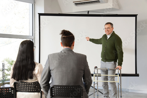 Male business speaker with walker near projector screen conducting seminar to...