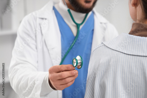 Male doctor with stethoscope listening to patient in clinic, closeup